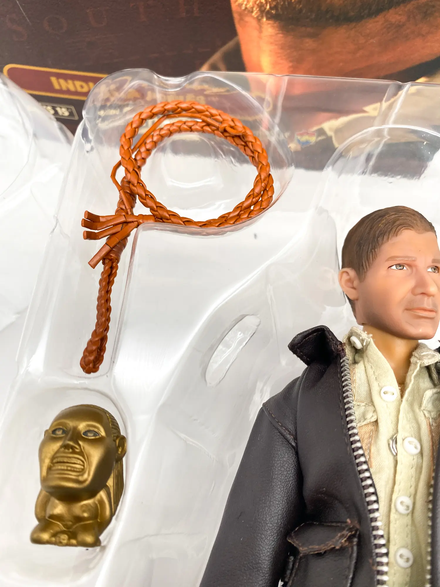 Détail du visage de la figurine Indiana Jones, du fouet tressé et de l’idole dorée.