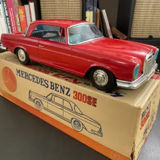 Front three-quarter view of the red Ichiko Mercedes-Benz 300SE friction tin car standing on its original box